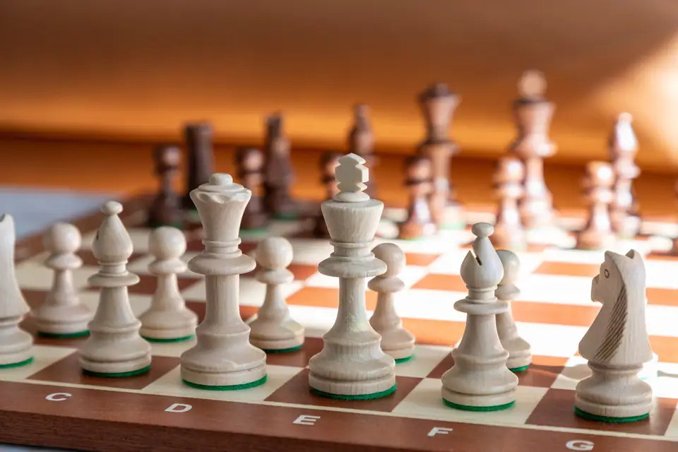White chess pieces lined up on a wooden chessboard, close up