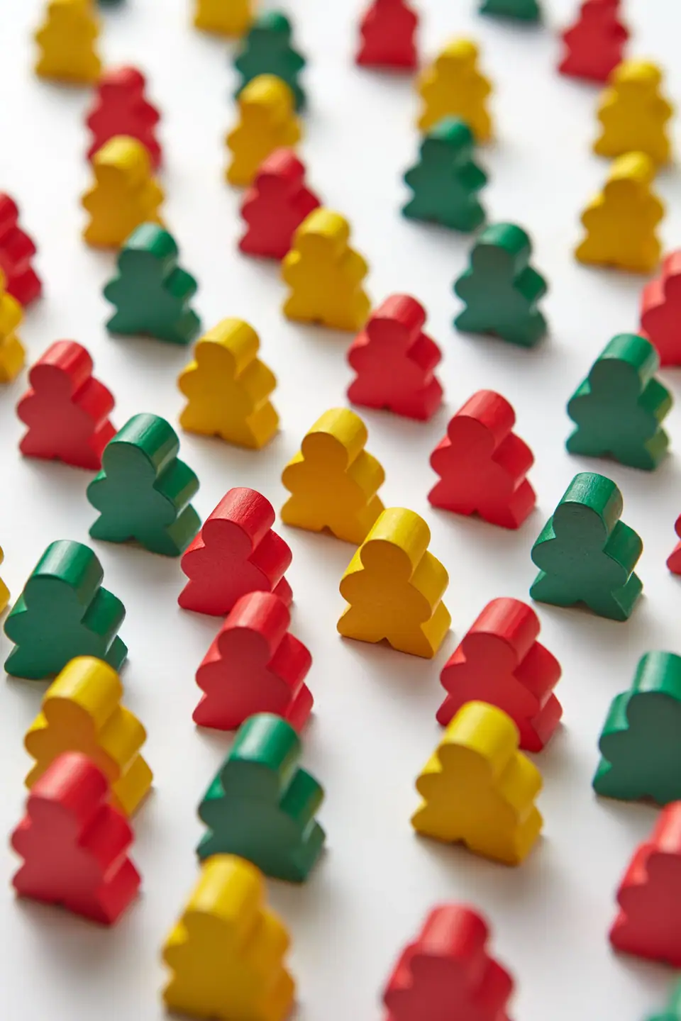 A pile of red, green and yellow wooden meeples on a white table